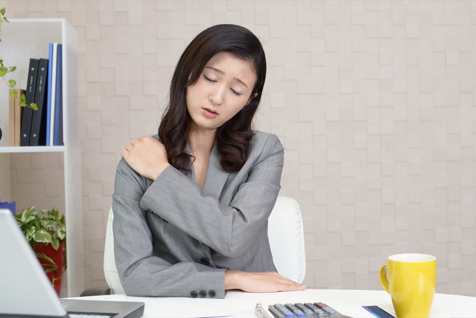 オフィスのデスクで肩を押さえて顔をしかめる女性