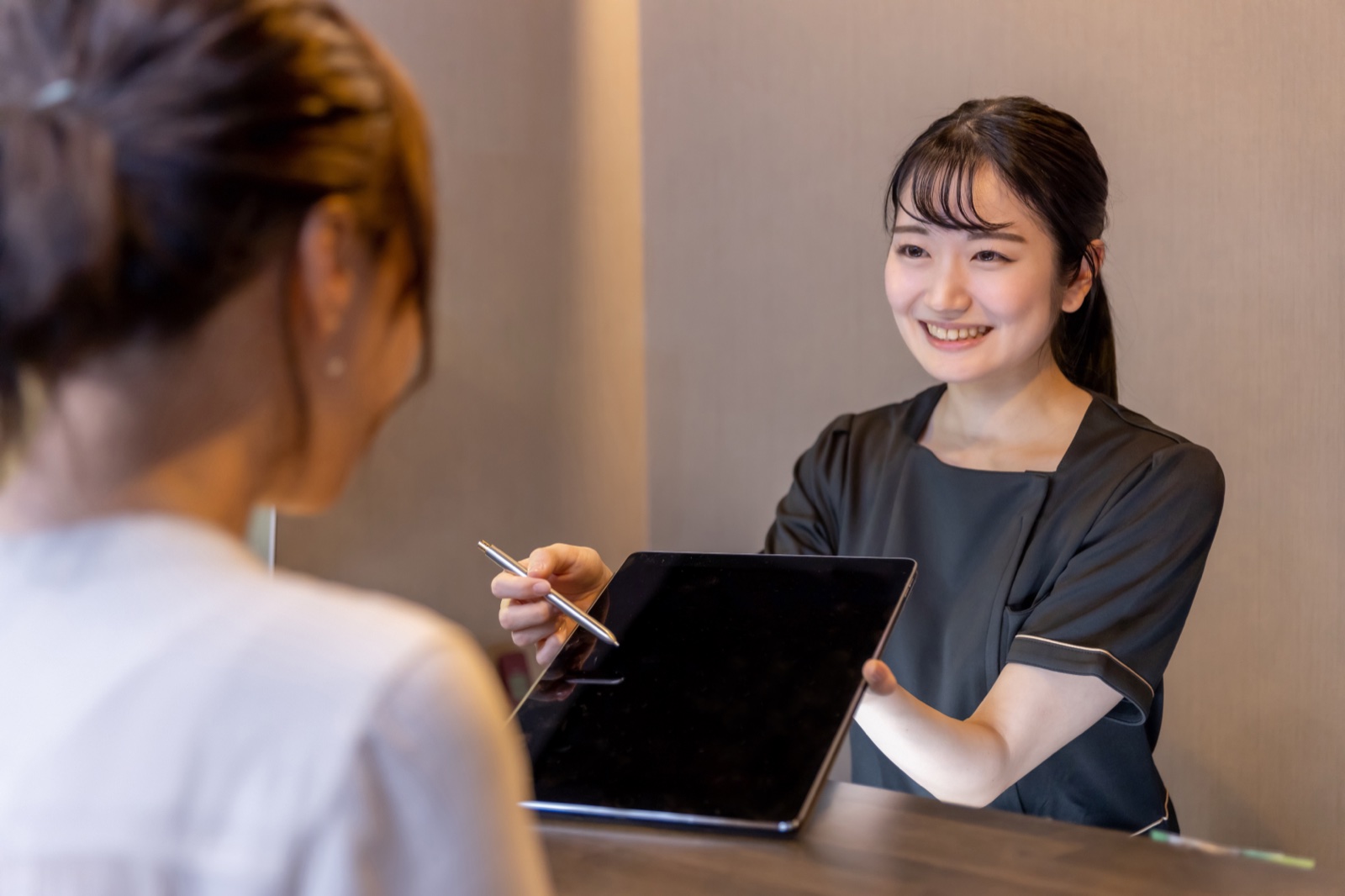 受付カウンターでタブレットを見せながら説明する女性スタッフ
