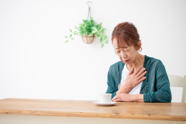 テーブルで胸に手を当てて顔をしかめる年配の女性