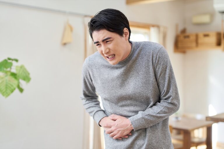 室内でおなかを両手で押さえて顔をしかめる男性