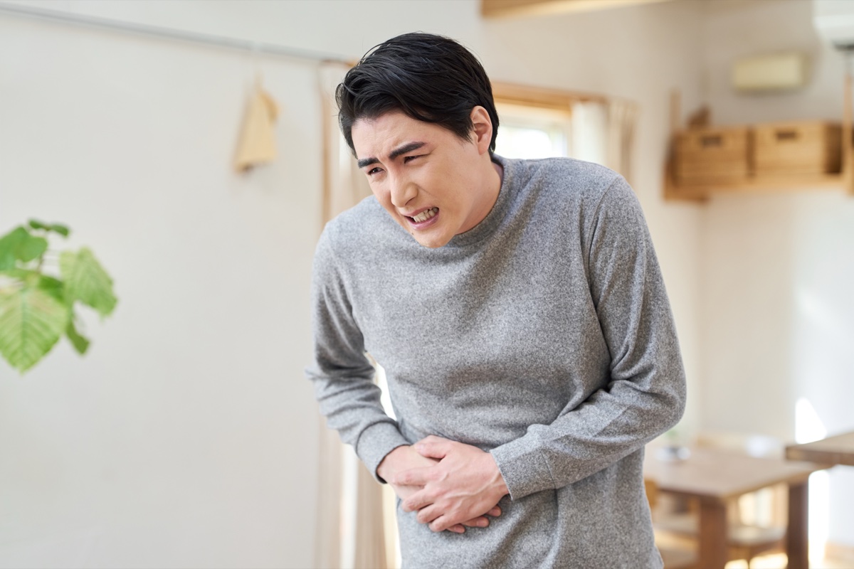 室内でおなかを両手で押さえて顔をしかめる男性