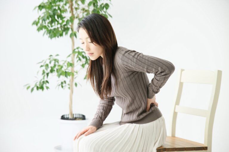 茶色のニット姿で椅子から立ち上がり腰に手を当てる女性