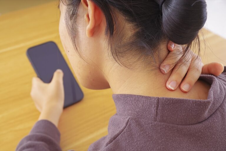 スマートフォンを持ちながら首の付け根に手を当てる女性