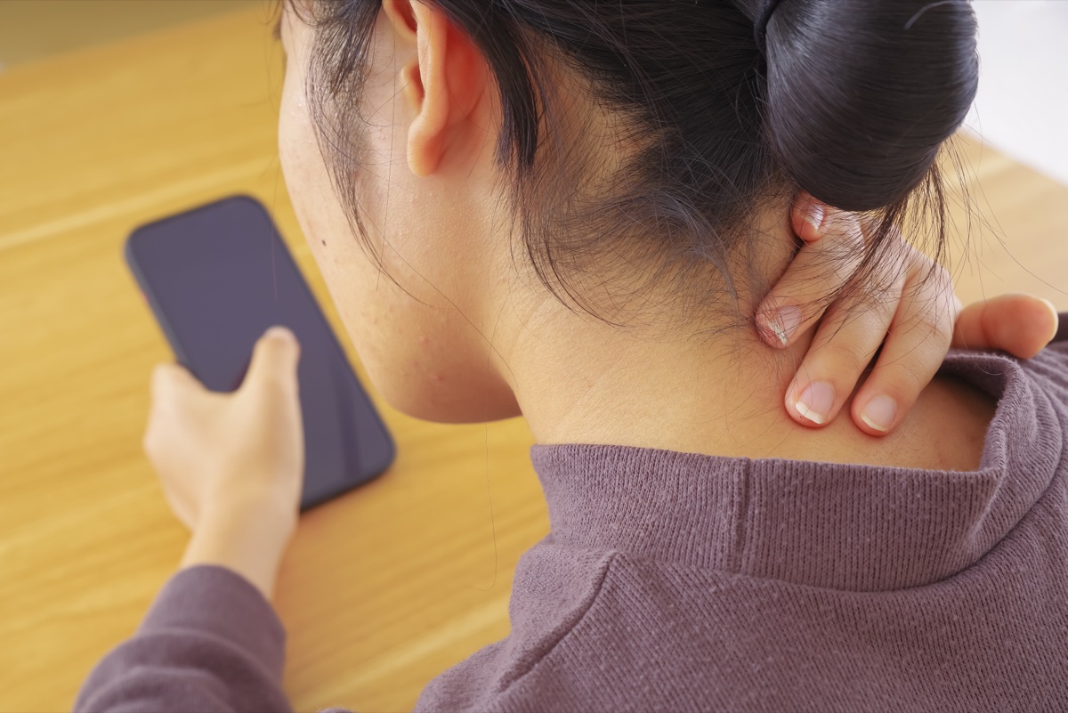 スマートフォンを持ちながら首の付け根に手を当てる女性