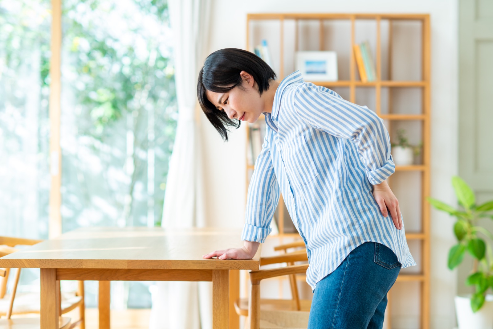 テーブルに手をついて腰を押さえる女性