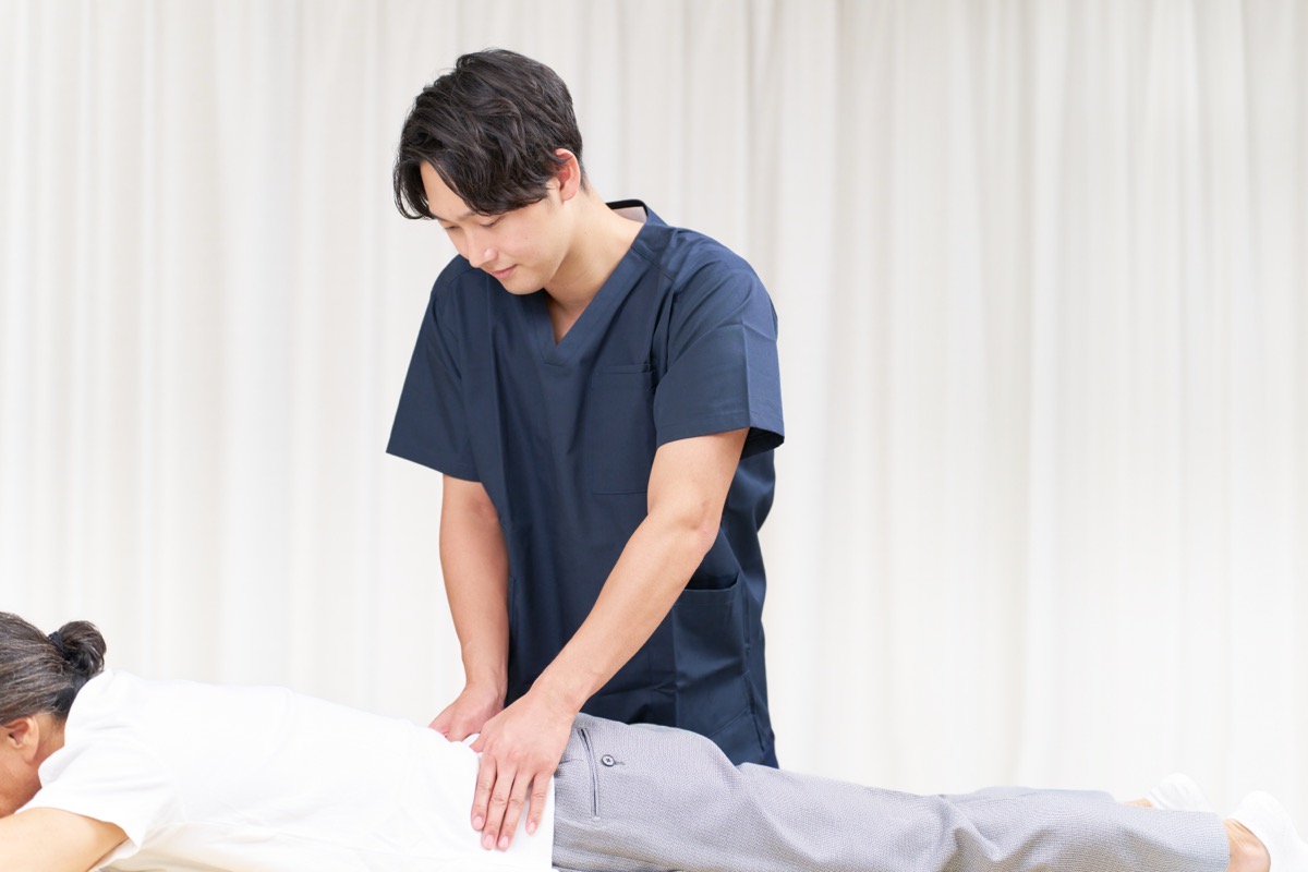 施術ベッドでうつぶせの患者の腰に手を当てる施術者