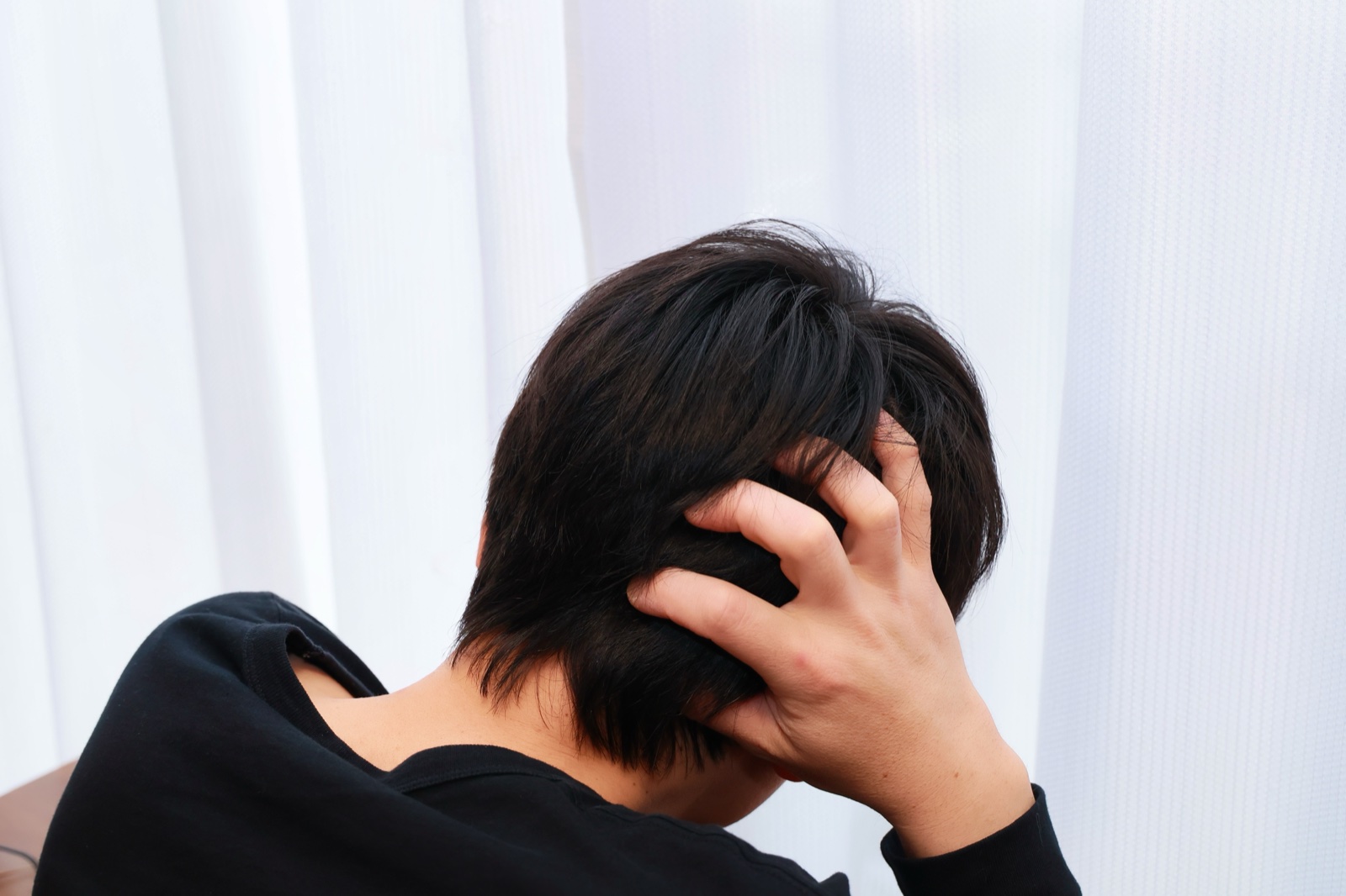 黒い服の男性が後ろ向きで後頭部に手を当ててうつむく姿