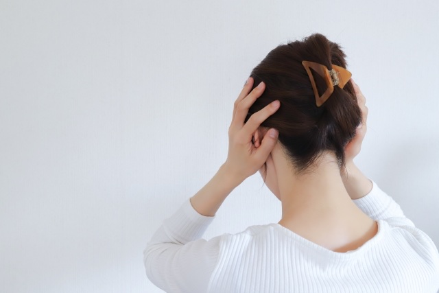 白いニットの女性が後ろ向きで両手を後頭部に当てる姿