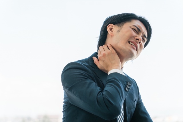 スーツ姿で首の横を押さえて顔をしかめる男性