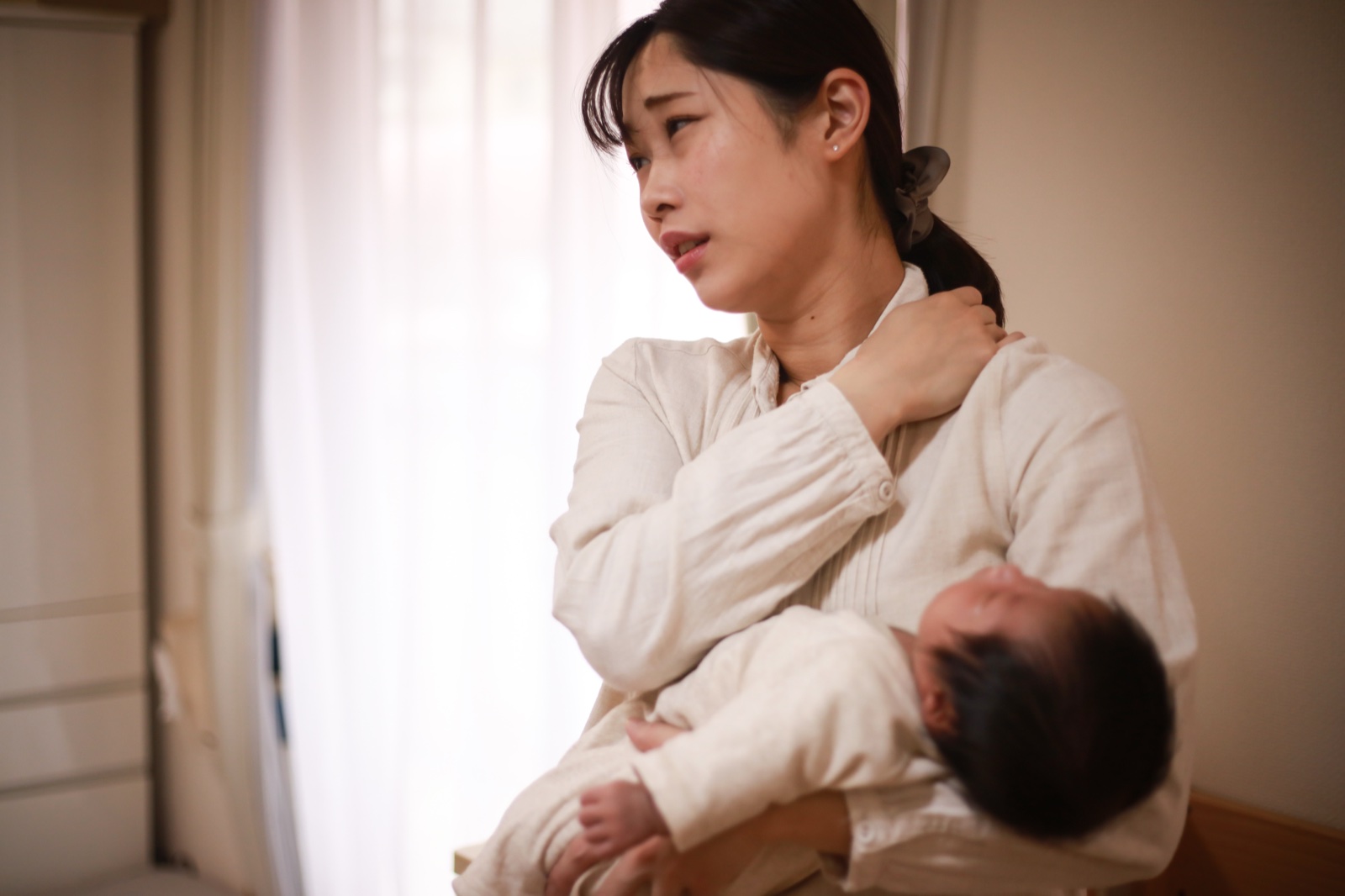新生児を抱いたまま片手で肩をつかみ顔をしかめる女性