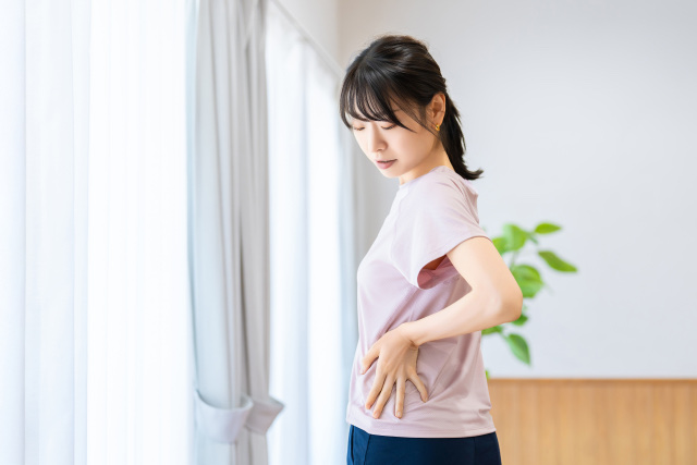 窓辺でうつむき、腰の横に手を当てる女性