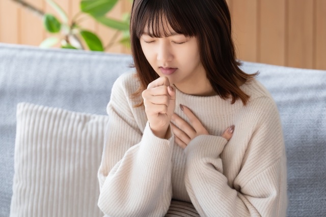 ソファで口元にこぶしを当てて咳き込む女性