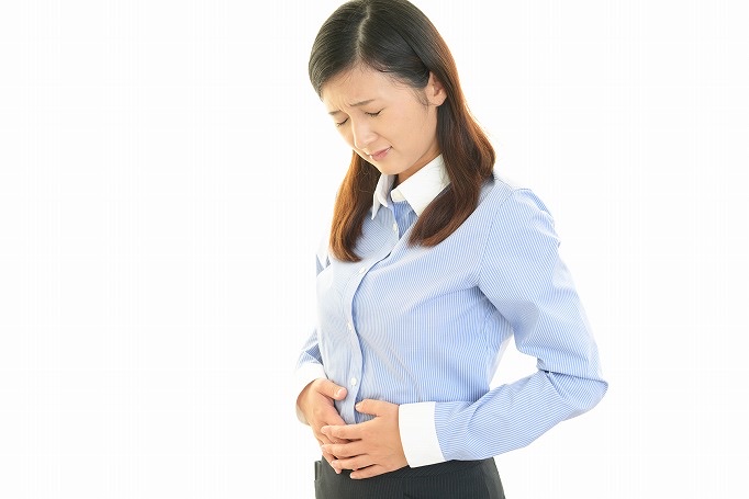 おなかを両手で押さえて顔をしかめるストライプのシャツの女性